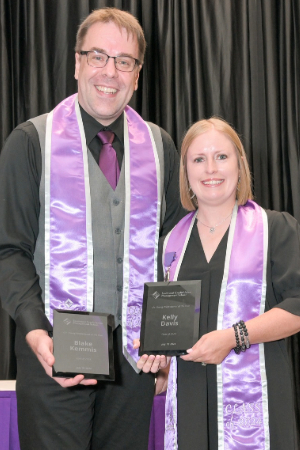 Two people wearing purple graduation stoles holding plaques and smiling.