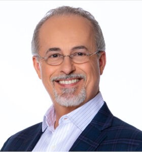 Smiling person with oval rimless glasses, gray hair and a goatee who is wearing a sport jacket and unbuttoned striped collared shirt. 