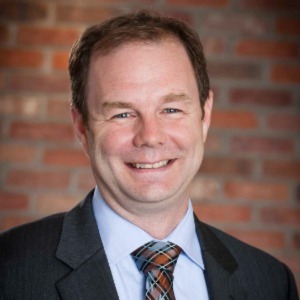 Smiling man with a plaid tie, collared shirt and dark suit jacket